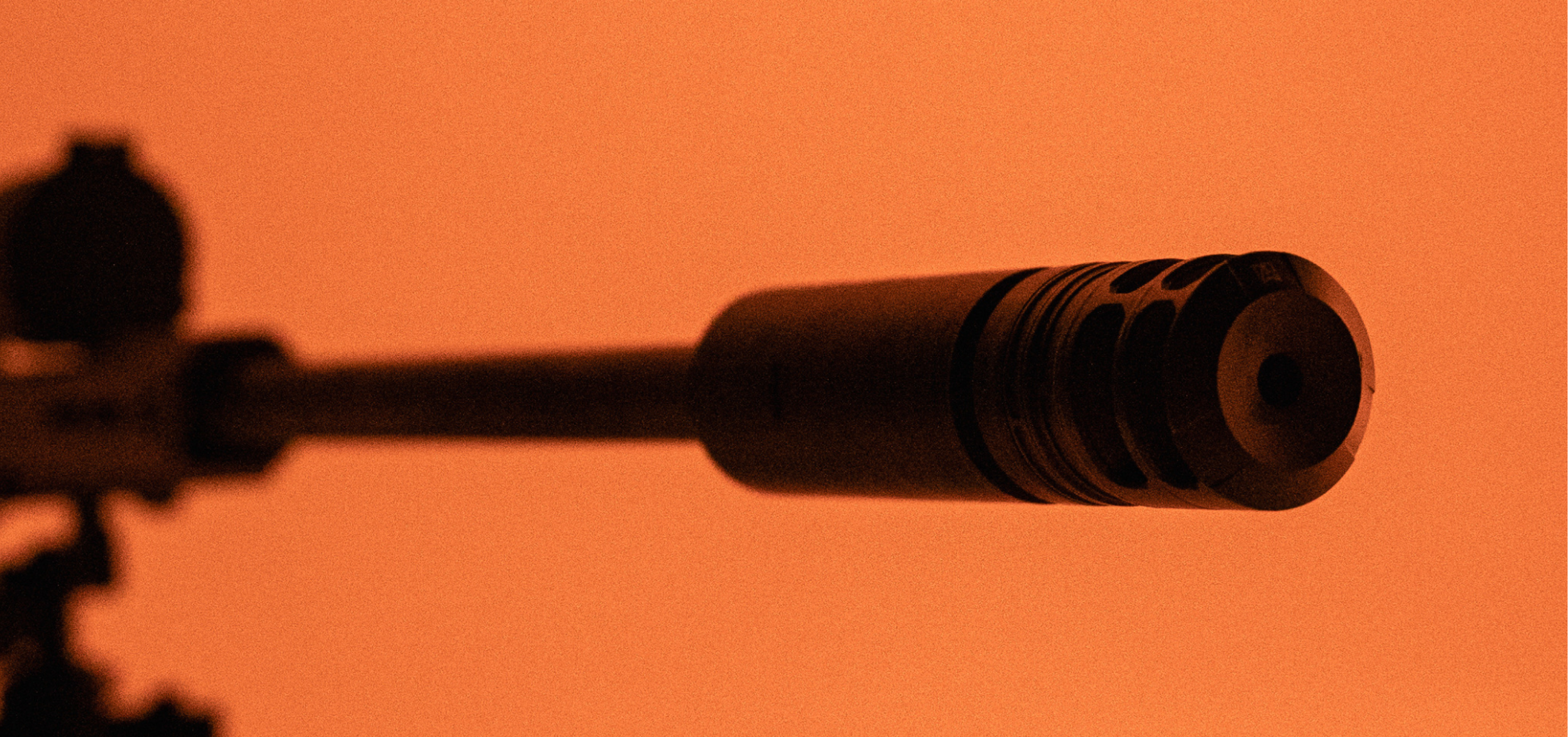 Close-up of a rifle scope and barrel on an orange background